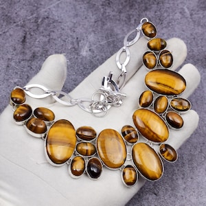 Op de afbeelding: Een zilverkleurige ketting met ovale en ronde tijgeroog edelstenen. De ketting heeft een toggle sluiting en een ketting van onderling verbonden schakels. De tijgeroog stenen zijn bruin en goud.