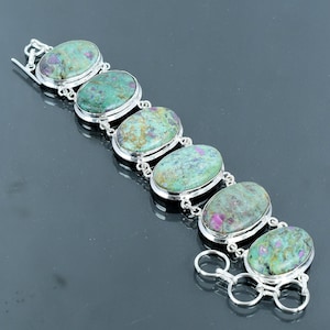 May include: A silver bracelet with oval-shaped green and pink gemstones. The bracelet has a clasp closure.