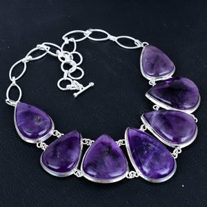 May include: A silver necklace with a teardrop-shaped amethyst pendant. The necklace has a silver chain and a lobster clasp.