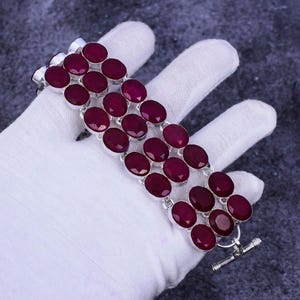 May include: A silver bracelet with multiple rows of round, red gemstones. The bracelet has a toggle clasp.