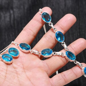 May include: A silver necklace and earrings set with oval-shaped blue topaz gemstones. The necklace has a delicate chain and the earrings are drop style.