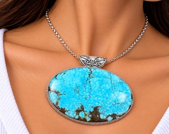 May include: A large oval turquoise pendant featuring a vibrant blue stone with dark brown matrix veining. The stone is set in a detailed silver frame with a decorative bail, suspended from a silver wheat chain necklace.