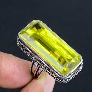 May include: A silver ring featuring a large, rectangular, light green gemstone. The ring has an ornate, filigree design.