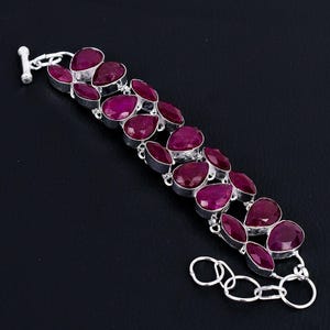 May include: A silver bracelet featuring multiple oval-shaped, deep red gemstones. The gemstones are set in individual silver settings and connected by silver links. The bracelet has a toggle clasp closure.