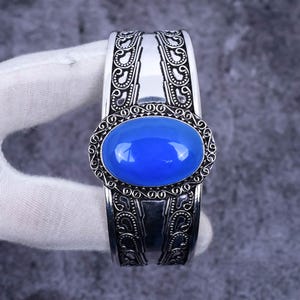 May include: A silver cuff bracelet with an ornate design and a large blue oval gemstone in the centre.