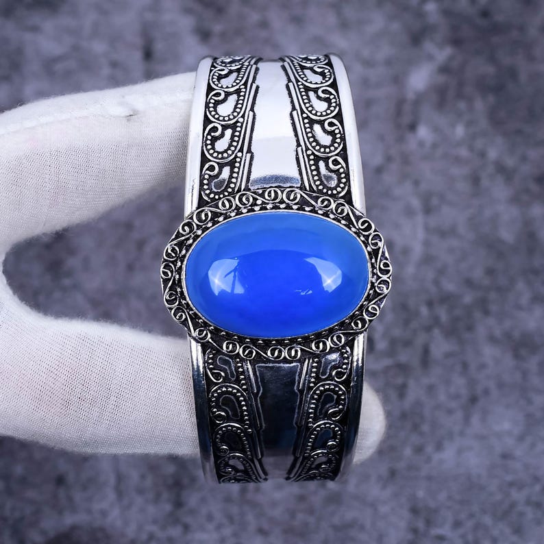 May include: A silver cuff bracelet with an ornate design and a large blue oval gemstone in the centre.