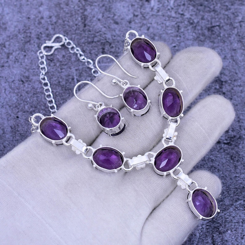 May include: A silver necklace and earrings set with purple oval-shaped gemstones. The necklace has a pendant with a larger gemstone.