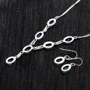 May include: A silver necklace with a pendant featuring a cluster of blue gemstones. The necklace is paired with matching earrings with a single blue gemstone.