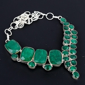 Puede incluir: Un collar de plata con un colgante de piedra preciosa verde. El colgante está formado por varias piedras grandes de forma rectangular y piedras redondas más pequeñas. El collar está adornado con una cadena de plata.