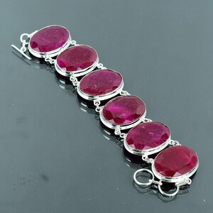 May include: A silver bracelet with six oval-shaped ruby gemstones. The bracelet has a lobster clasp closure.