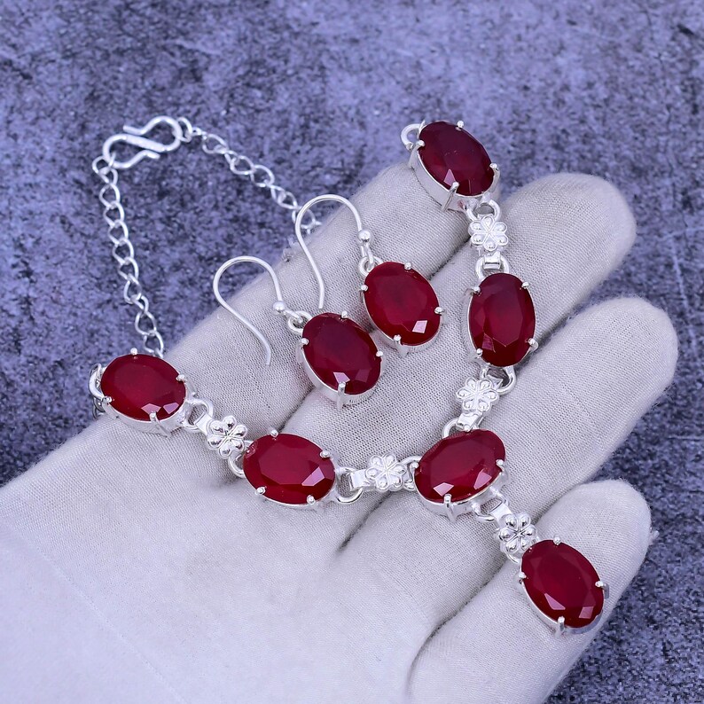 May include: A silver necklace and earrings set with red oval-shaped gemstones. The necklace has a pendant with a larger gemstone and a chain with smaller gemstones.
