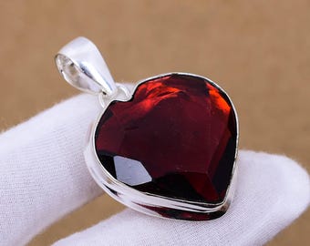 May include: A silver heart-shaped pendant with a large, faceted, dark red gemstone.