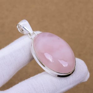 May include: A silver pendant featuring a large oval-shaped pink rose quartz gemstone. The pendant is set in a silver bezel and has a bail for attaching a chain.