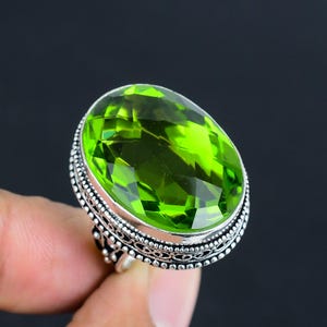 Könnte beinhalten: Ein silberner Ring mit einem großen, ovalen, grünen Edelstein. Der Ring hat ein kompliziertes, detailliertes Design um den Edelstein herum.