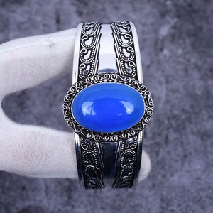 May include: A silver cuff bracelet with an ornate design and a large blue oval gemstone in the centre.