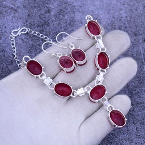 May include: A silver necklace and earrings set with red oval-shaped stones. The necklace has a pendant with a larger red stone.
