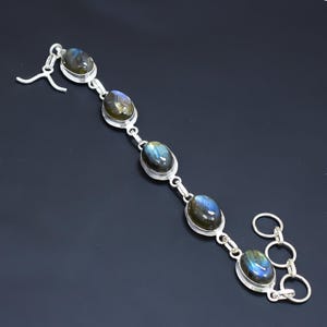 May include: A silver bracelet with five oval-shaped labradorite gemstones. The bracelet has a lobster claw clasp and a chain extender.