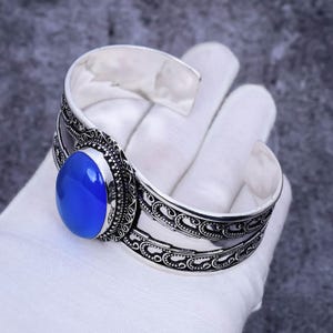May include: Silver cuff bracelet with an ornate design and a large oval blue gemstone.