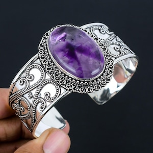 Op de afbeelding: Een zilveren armband met een sierlijk ontwerp en een grote ovale amethist edelsteen.