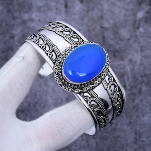 May include: A silver cuff bracelet with an ornate design and a large blue oval gemstone.
