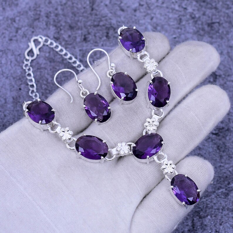 May include: A silver necklace and earrings set with purple amethyst gemstones. The necklace features a pendant with a single amethyst stone and the earrings have a single amethyst stone each.