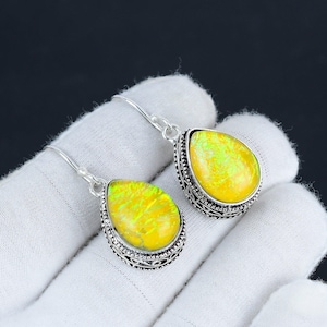 Puede incluir: Un par de pendientes de plata con piedras de ópalo amarillo en forma de lágrima. Los pendientes tienen un diseño filigranado intrincado alrededor de las piedras.