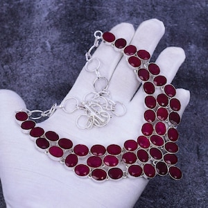 May include: A silver necklace featuring a double row of oval-shaped, deep red gemstones. The necklace has a lobster clasp fastening and an extender chain.