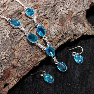 May include: A silver necklace and earrings set with blue oval-shaped gemstones. The necklace has a long pendant with a larger gemstone.