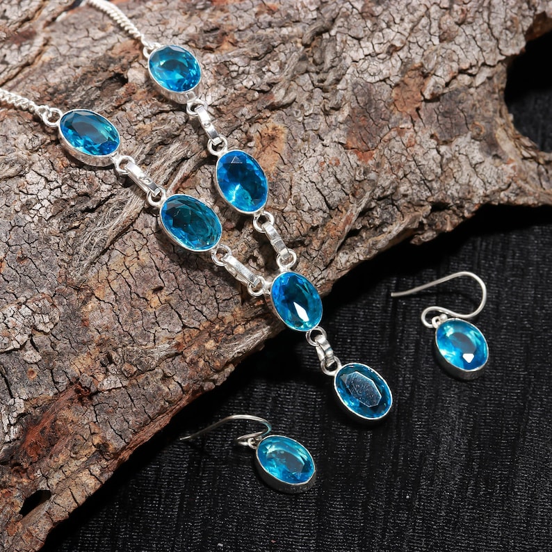 May include: A silver necklace and earrings set with blue oval-shaped gemstones. The necklace has a long pendant with a larger gemstone.
