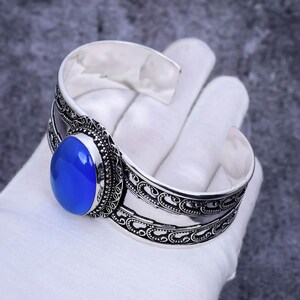 May include: Silver cuff bracelet with an ornate design and a large oval blue gemstone.