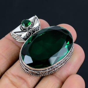 Puede incluir: Un colgante de plata con una gran piedra preciosa verde de forma ovalada. El colgante está adornado con intrincados detalles de plata alrededor de la piedra preciosa.