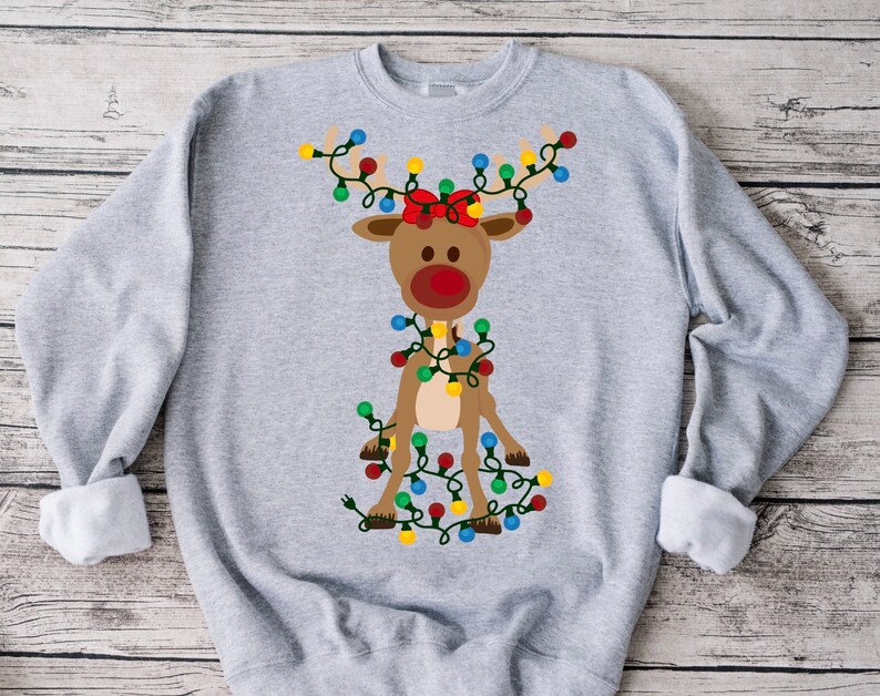 K&ouml;nnte beinhalten: Ein graues Sweatshirt mit einem Cartoon-Rentier, das eine rote Schleife tr&auml;gt und in bunten Weihnachtslichtern verheddert ist.