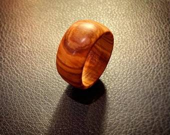 Puede incluir: Un anillo de madera con un patrón de veta de madera natural. El anillo es marrón y tiene un acabado liso y pulido.