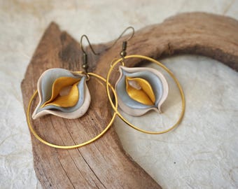 May include: A pair of dangle earrings featuring gold-tone metal hoops and layered, petal-like shapes in shades of beige, grey, and metallic gold. The earrings are suspended from dark metal hooks and include a small, light-colored stone accent.