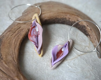May include: A pair of hoop earrings featuring sculpted, organic-shaped pendants in shades of lavender, mauve, and tan. Each pendant has a glossy, reddish-brown center accent and a small, iridescent white bead embedded within the layered, folded structure.