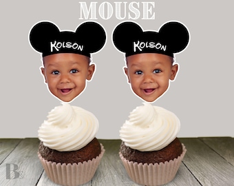 Può includere: Due cupcake con glassa bianca e orecchie di Topolino nere con il nome Kolsen su di esse. I cupcake sono su una superficie di legno marrone.