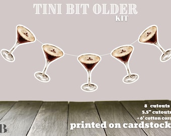 Op de afbeelding: Een feestbanner met acht 14 cm uitsnijdingen van espresso martini's, gedrukt op karton. De banner is aan elkaar geregen met een 1,80 meter katoenen koord. De banner luidt "Tini Bit Older Kit".