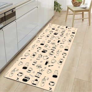 May include: A beige kitchen runner rug with a black and white coffee themed pattern. The pattern includes coffee cups, coffee beans, coffee pots, and the word "Coffee".
