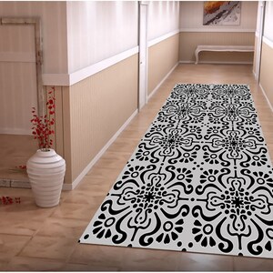 May include: Black and white patterned runner rug with a geometric design. The rug is laid out in a hallway with white walls and a wooden floor.
