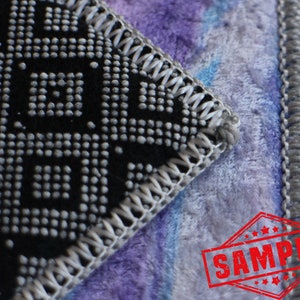 May include: Close-up of a black and gray patterned fabric with a gray stitched border. The fabric is sewn to a purple and blue fuzzy fabric with a gray stitched border. The image has a red stamp that says "SAMPLE" in white letters.
