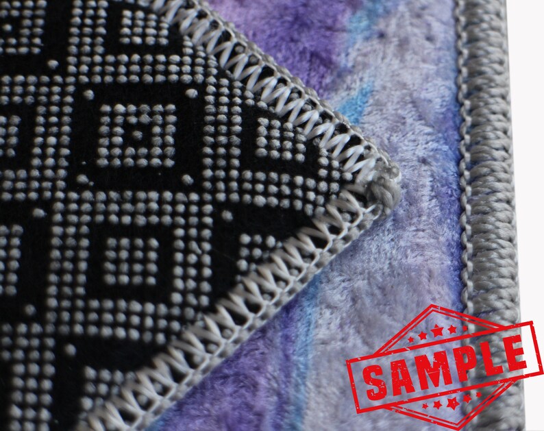 May include: Close-up of a black and gray patterned fabric with a gray stitched border. The fabric is sewn to a purple and blue fuzzy fabric with a gray stitched border. The image has a red stamp that says "SAMPLE" in white letters.