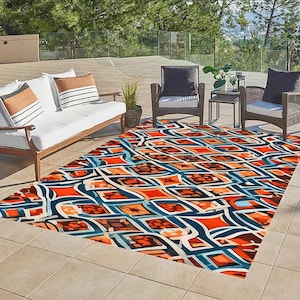 May include: A colorful geometric patterned rug with orange, blue, and white colors. The rug is laid out on a patio with outdoor furniture.