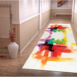 May include: A colourful abstract runner rug with a white background and brushstrokes of red, orange, yellow, green, purple, and black. The rug is laid out in a hallway with white walls and a wooden floor.