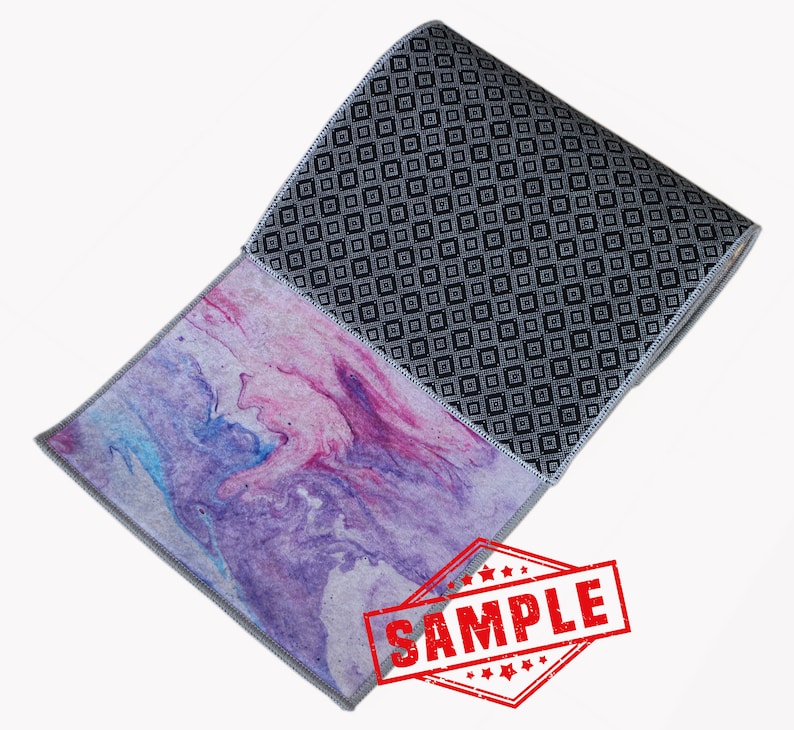 May include: A rolled up runner rug with a geometric pattern on one side and a pink and purple marbled pattern on the other side. The rug has a gray border and the word "SAMPLE" is stamped in red on the rug.