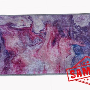 May include: Purple and pink abstract marbled area rug with a gray border. The rug has a sample label on it.