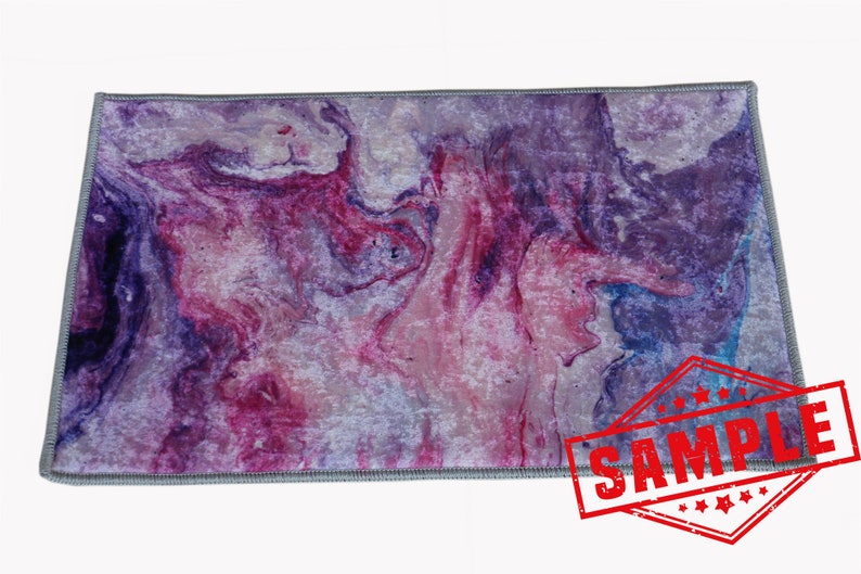 May include: Purple and pink abstract marbled area rug with a gray border. The rug has a sample label on it.