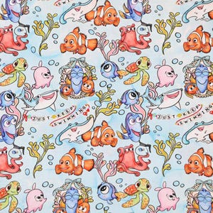 May include: A light blue fabric featuring a repeating pattern of cartoon sea creatures, including clownfish, blue tangs, sea turtles, and sharks. The phrase "Just Keep Swimming" is also included in the design. The overall theme is aquatic.