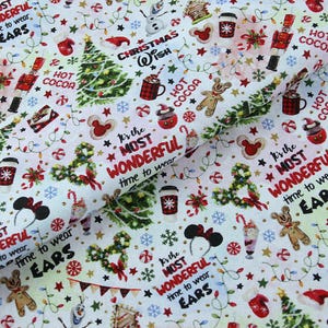 Może przedstawiać: Biała tkanina z świątecznym wzorem bożonarodzeniowym. Wzór zawiera choinki, uszy Myszki Miki, płatki śniegu i napis "It's the MOST WONDERFUL time to wear". Inne elementy to kubki gorącej czekolady i piernikowe ludziki.
