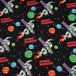 Puede incluir: Tela negra con un patrón repetido de un personaje de guardabosques espacial con un traje espacial blanco y verde con alas moradas. El diseño incluye planetas en azul, verde y naranja, y el texto "SPACE RANGER" en rojo.