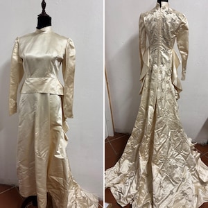 May include: A vintage ivory satin wedding dress with long sleeves and a high neckline. The dress features a fitted bodice, a peplum waist, and a flowing skirt with a train. The back of the dress is embellished with floral embroidery and small embellishments.